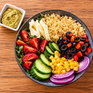 Bol vegetarian cu bulgur, mozzarella, rucola, roșii cherry, castraveți, porumb, măsline, ardei și ceapă roșie, cu sos pesto alături